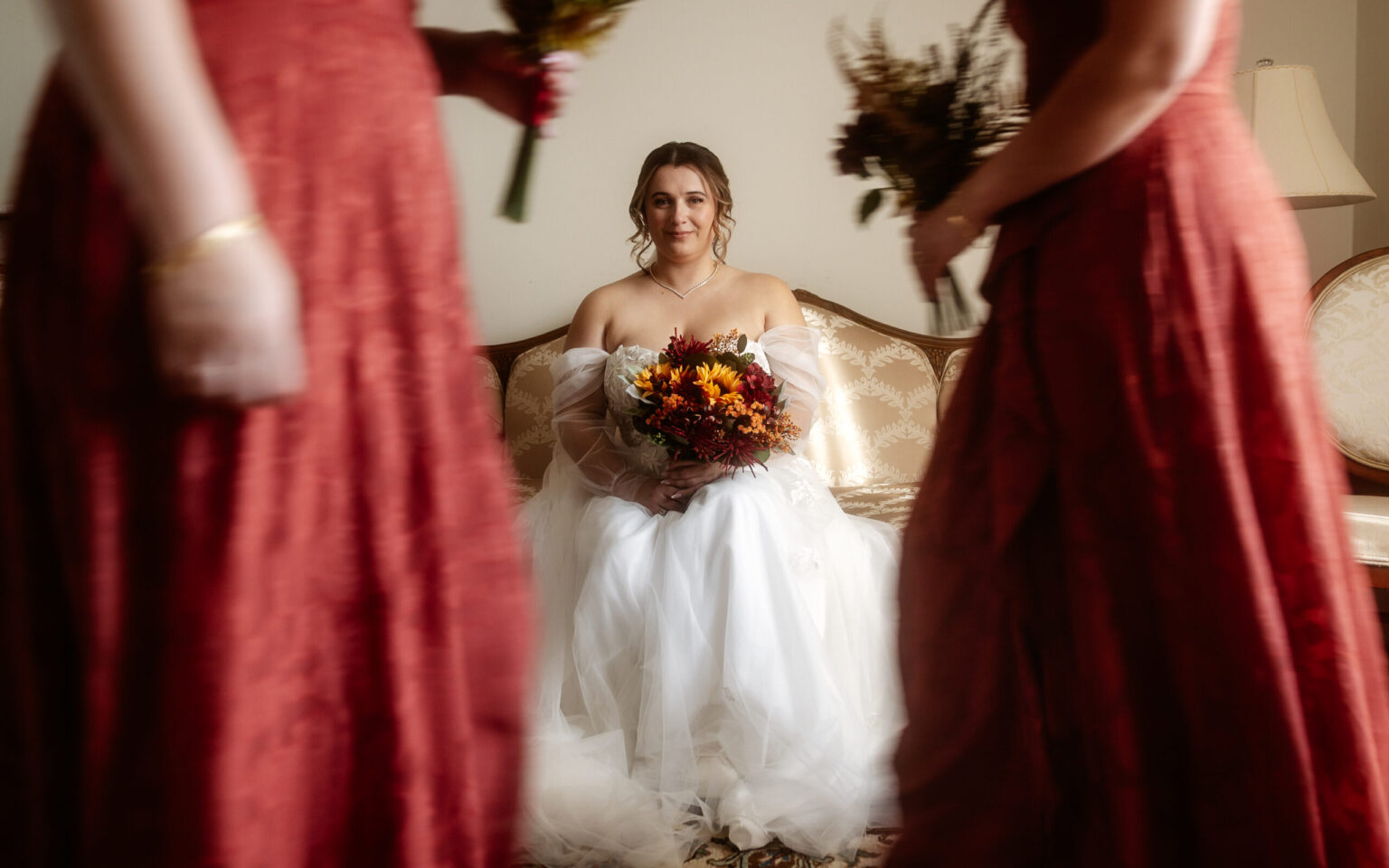 Mariée assise avec son bouquet entre deux demoiselles d'honneur en robes rouges